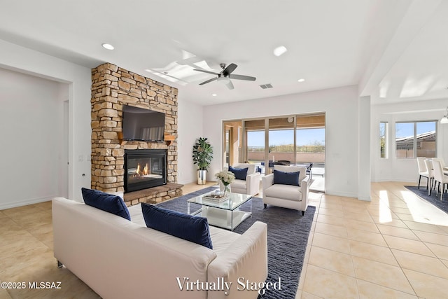 tiled living room with ceiling fan and a stone fireplace