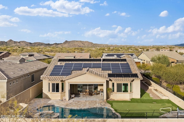 back of property with a mountain view, solar panels, a patio, and a fenced in pool