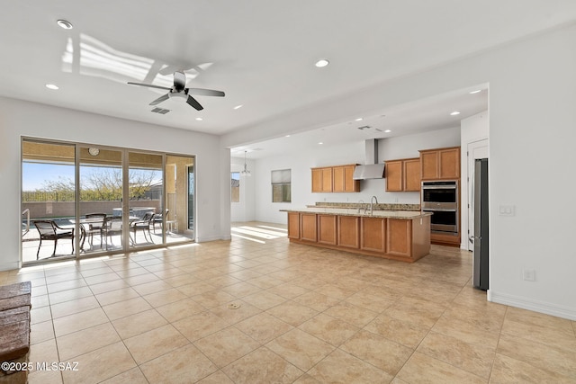 kitchen with light stone countertops, sink, stainless steel appliances, wall chimney range hood, and an island with sink