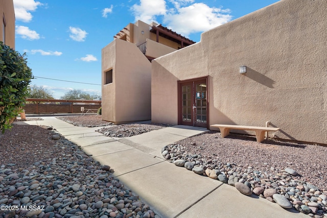 entrance to property with stucco siding, french doors, and fence