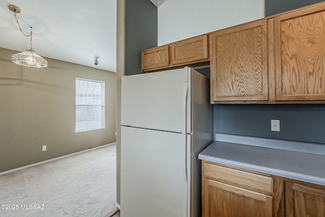 kitchen featuring light carpet, baseboards, hanging light fixtures, freestanding refrigerator, and brown cabinetry