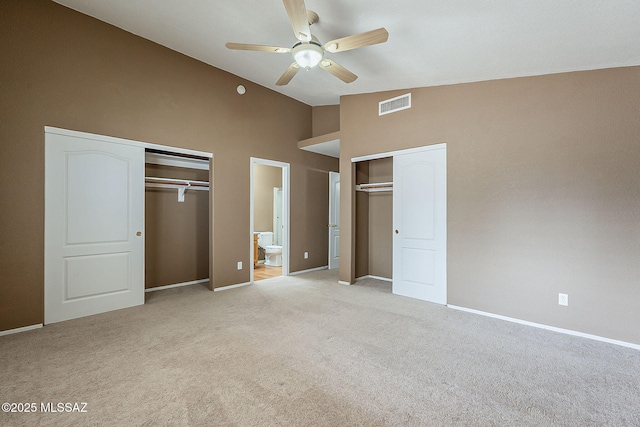 unfurnished bedroom with visible vents, light colored carpet, ensuite bathroom, vaulted ceiling, and multiple closets