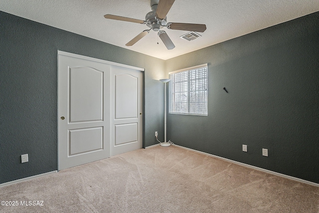 unfurnished bedroom with a textured ceiling, a textured wall, visible vents, a closet, and carpet