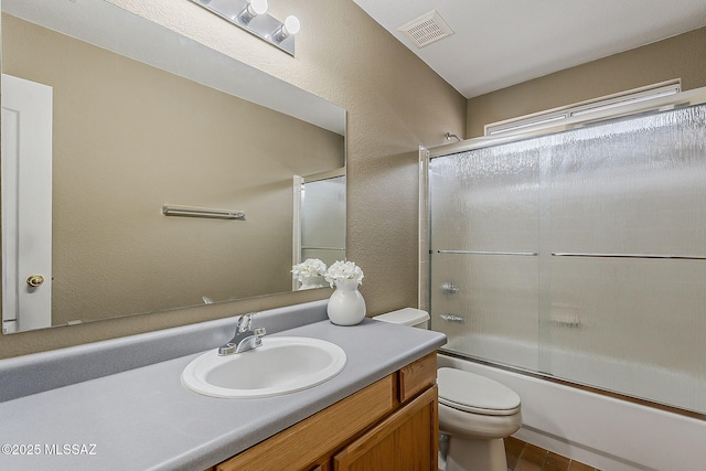 bathroom with visible vents, a textured wall, toilet, enclosed tub / shower combo, and vanity