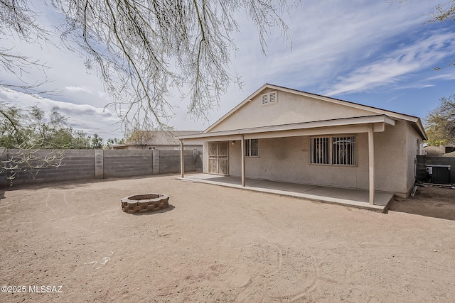 rear view of property featuring stucco siding, an outdoor fire pit, central AC, a patio area, and a fenced backyard