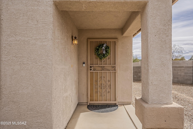 view of exterior entry featuring fence and stucco siding