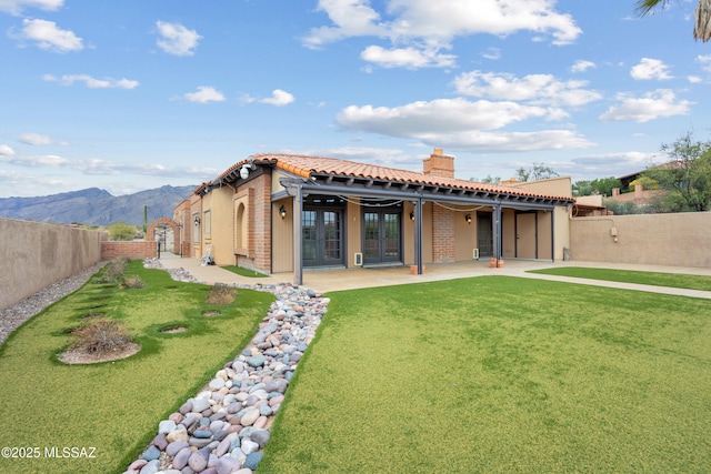 back of property with a mountain view, french doors, a patio, and a lawn