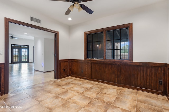 empty room featuring ceiling fan, french doors, and wood walls