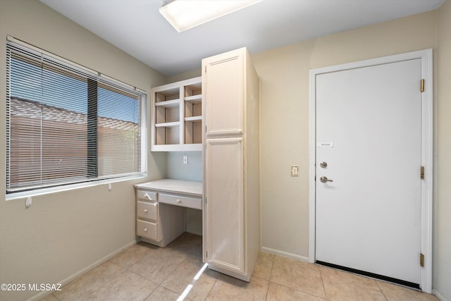 unfurnished office featuring light tile patterned floors, built in desk, and baseboards