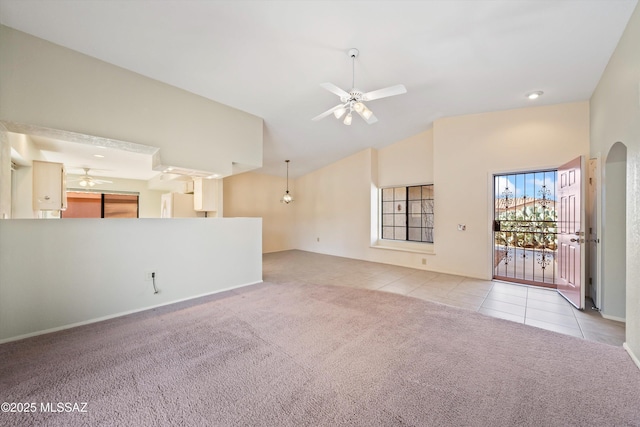 unfurnished living room with ceiling fan, arched walkways, tile patterned flooring, carpet flooring, and vaulted ceiling