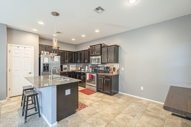 kitchen with a center island with sink, sink, stone countertops, dark brown cabinetry, and stainless steel appliances
