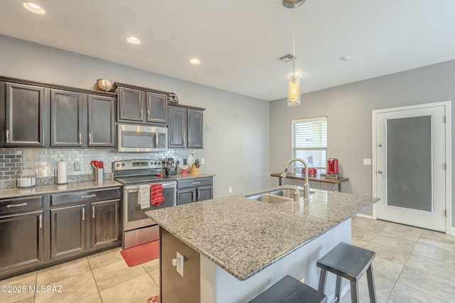 kitchen with pendant lighting, sink, light stone countertops, an island with sink, and stainless steel appliances