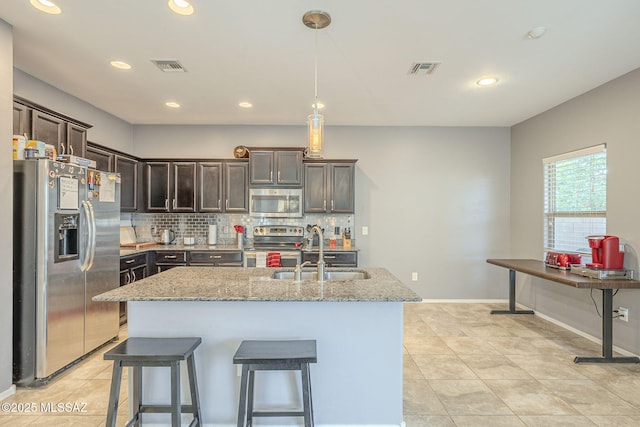 kitchen with light stone countertops, sink, a kitchen island with sink, and appliances with stainless steel finishes