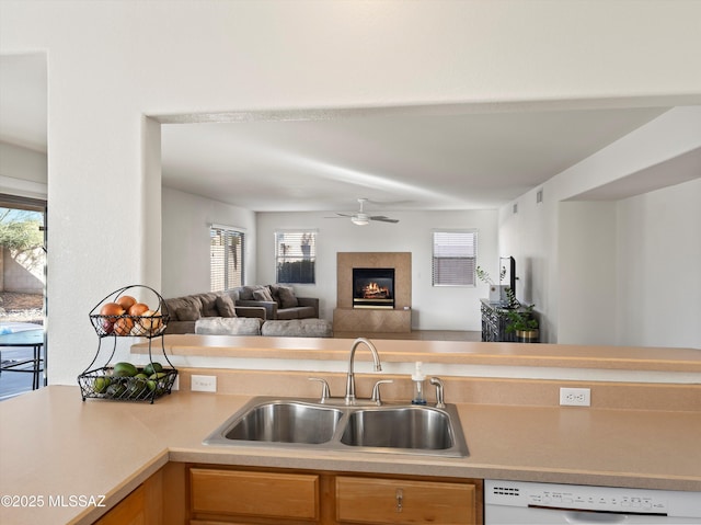 kitchen with a wealth of natural light, white dishwasher, a tiled fireplace, and sink