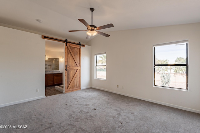 unfurnished bedroom featuring lofted ceiling, ensuite bath, ceiling fan, carpet flooring, and a barn door