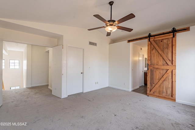 unfurnished bedroom with carpet floors, a barn door, ceiling fan, and vaulted ceiling