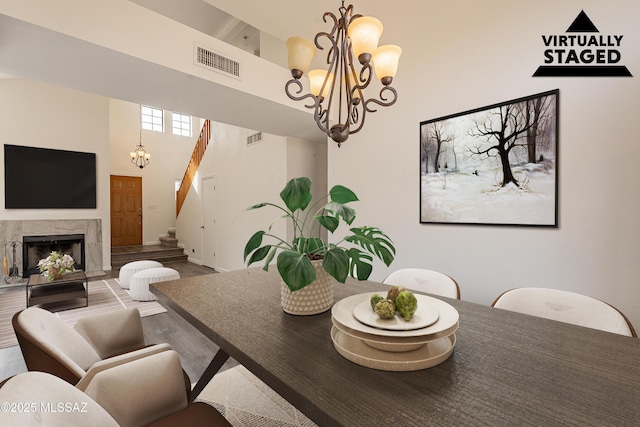 dining space featuring an inviting chandelier, a towering ceiling, wood-type flooring, and a premium fireplace