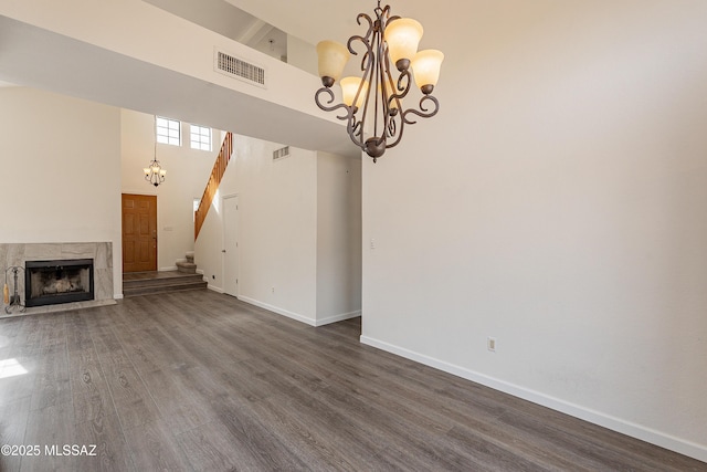 unfurnished living room featuring a high ceiling, dark wood-type flooring, a fireplace, and an inviting chandelier