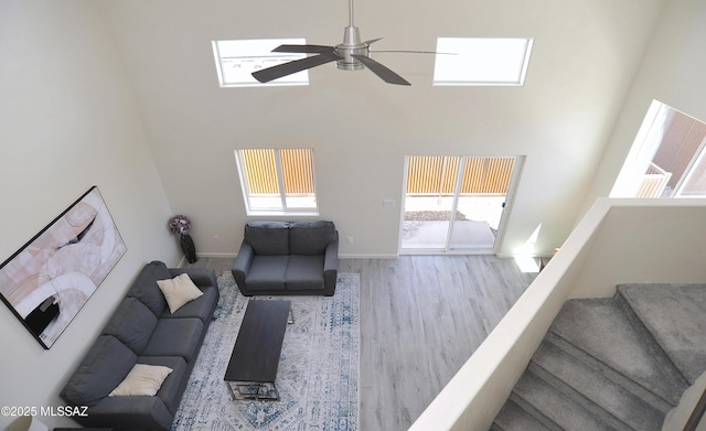 living room with ceiling fan, a towering ceiling, a healthy amount of sunlight, and wood-type flooring