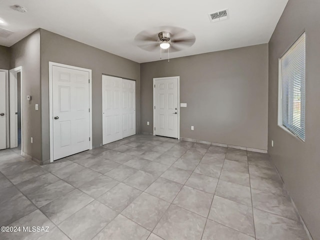 unfurnished bedroom with multiple closets, ceiling fan, and light tile patterned floors