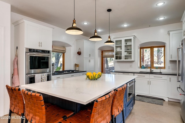 kitchen with hanging light fixtures, sink, white cabinets, a breakfast bar, and stainless steel appliances