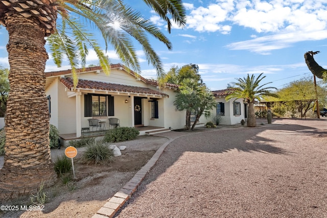 view of front facade featuring stucco siding, covered porch, driveway, and a tiled roof