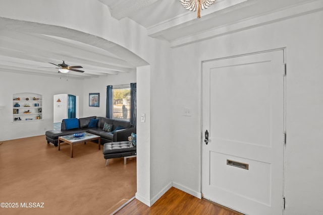 living room with beam ceiling, built in shelves, arched walkways, baseboards, and ceiling fan