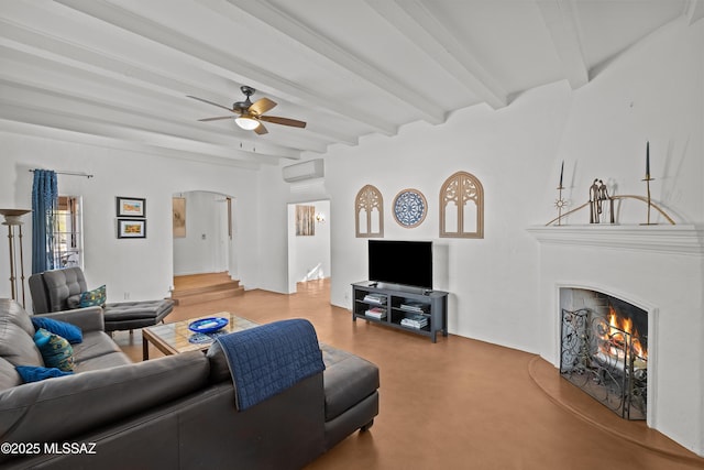 living area featuring beamed ceiling, an AC wall unit, a lit fireplace, arched walkways, and a ceiling fan