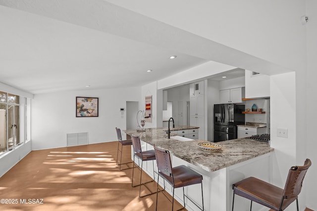 kitchen featuring a kitchen bar, visible vents, a sink, light stone counters, and black fridge with ice dispenser