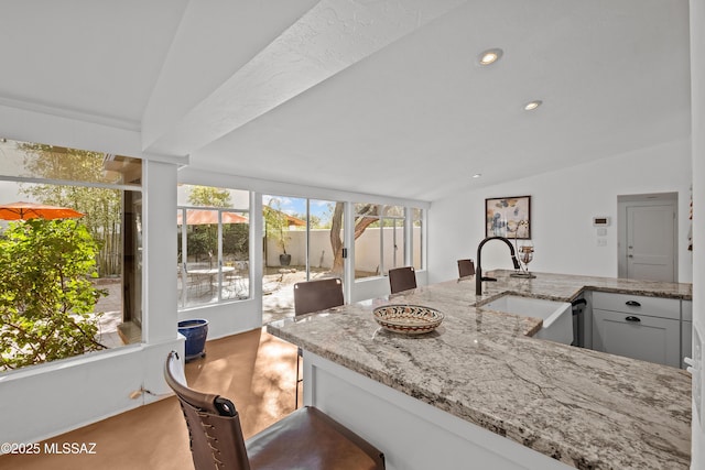 kitchen with lofted ceiling, light stone counters, recessed lighting, and a sink