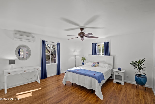 bedroom with a wall unit AC, wood finished floors, baseboards, and ceiling fan