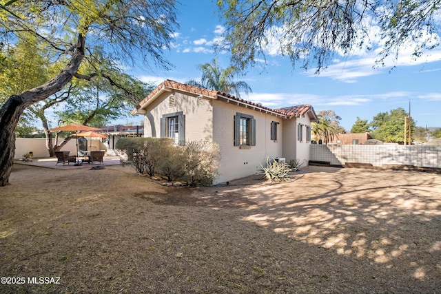 view of side of home featuring a patio, brick siding, a tile roof, and fence