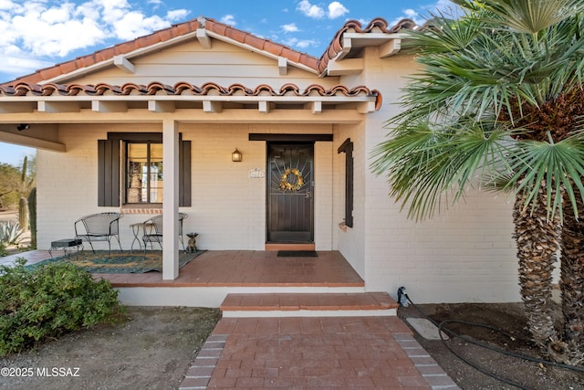 entrance to property with brick siding, covered porch, and a tile roof