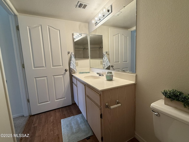 bathroom featuring vanity, wood finished floors, visible vents, a textured ceiling, and toilet