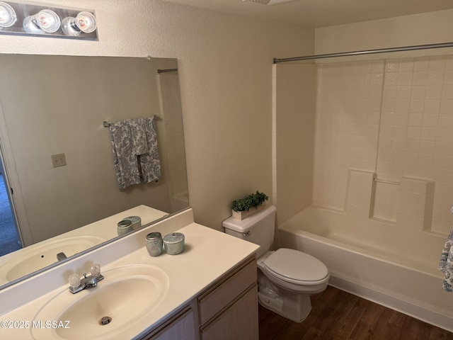 full bath featuring toilet, wood finished floors, bathtub / shower combination, vanity, and a textured wall