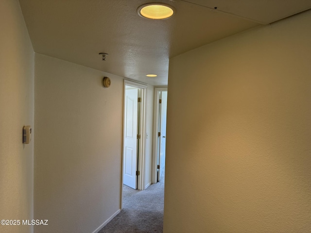 hallway featuring a textured ceiling, baseboards, and carpet