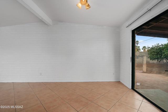 spare room featuring lofted ceiling with beams, light tile patterned floors, and brick wall