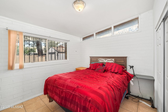 tiled bedroom with a closet, brick wall, and vaulted ceiling