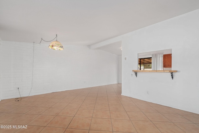 unfurnished room with lofted ceiling with beams, light tile patterned flooring, and brick wall