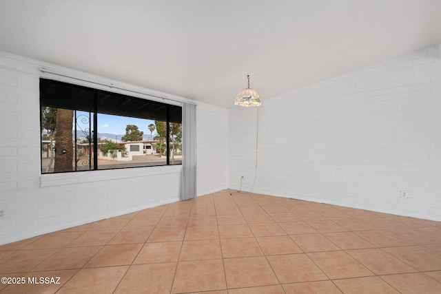 spare room featuring light tile patterned flooring and brick wall