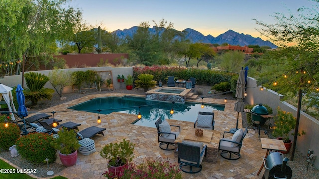 pool at dusk featuring an in ground hot tub, grilling area, a mountain view, and a patio area