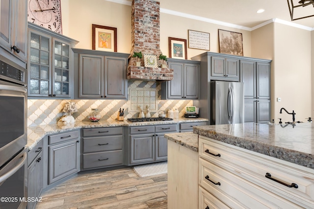 kitchen featuring stainless steel appliances, light stone counters, light wood-type flooring, decorative backsplash, and ornamental molding