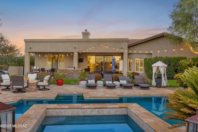 back house at dusk with a pool with hot tub and a patio