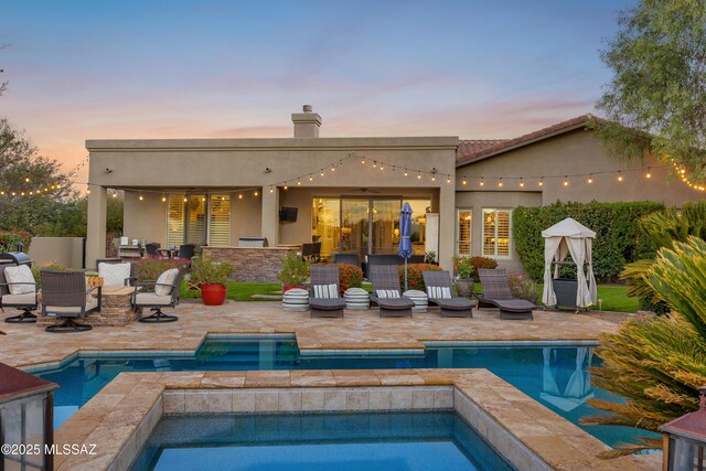 pool at dusk featuring an in ground hot tub and a patio area