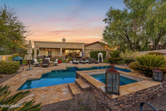 pool at dusk featuring area for grilling, an in ground hot tub, and a patio area