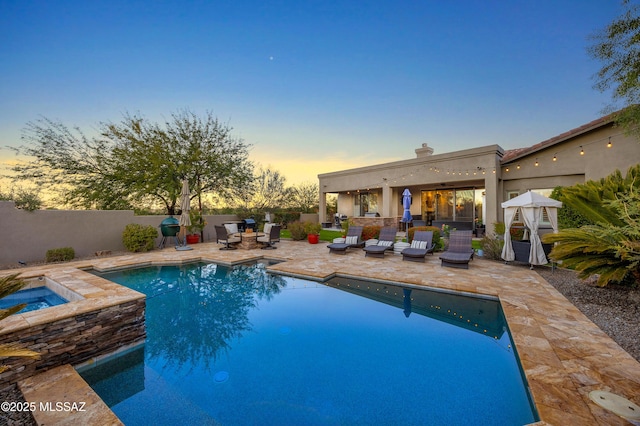 pool at dusk with an in ground hot tub and a patio