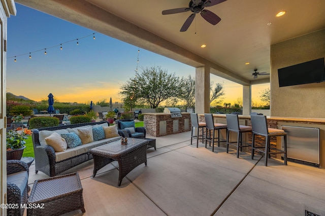 patio terrace at dusk featuring an outdoor living space, area for grilling, a bar, and ceiling fan