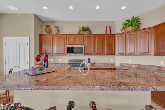 kitchen with a kitchen bar, light stone countertops, appliances with stainless steel finishes, and kitchen peninsula