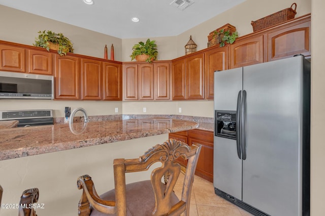 kitchen featuring stainless steel appliances, a kitchen breakfast bar, sink, light tile patterned flooring, and light stone counters