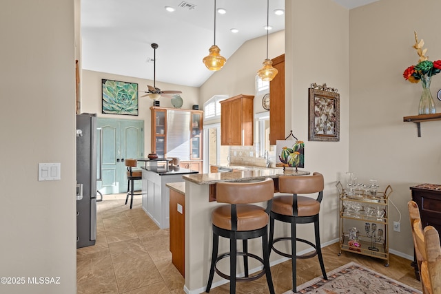 kitchen featuring stainless steel refrigerator, decorative light fixtures, a kitchen bar, light stone counters, and kitchen peninsula